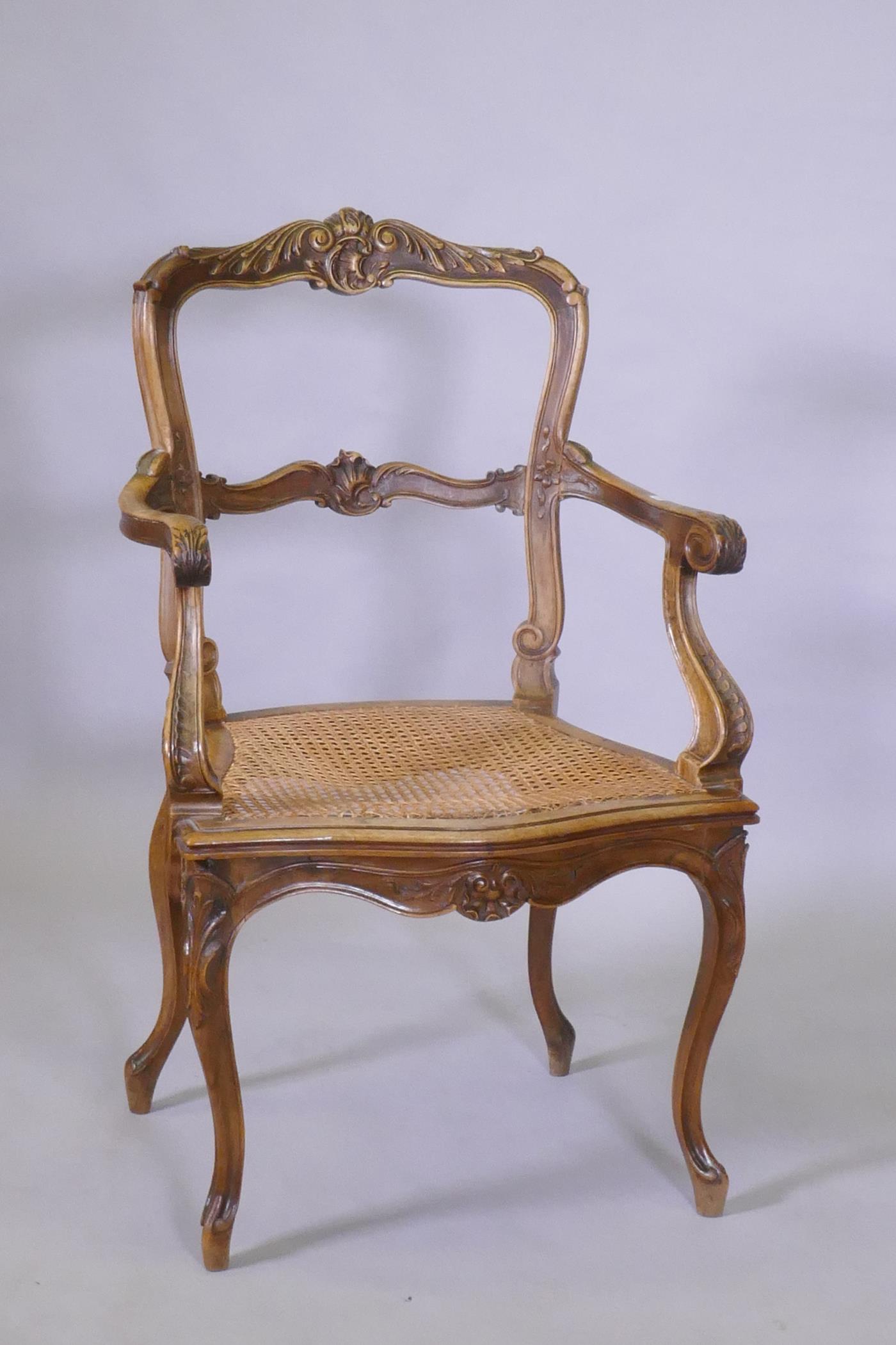 A C19th French carved walnut open arm chair with caned seat
