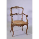 A C19th French carved walnut open arm chair with caned seat