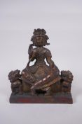 A Sino Tibetan bronze figure of a deity seated on a throne flanked by Fo-dogs, with remnants of gilt