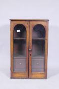 A Victorian mahogany hanging wall cupboard with two arched glazed doors, fitted with shelves and