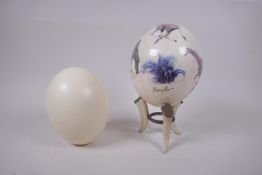 A decorative gilt and collage ostrich egg on stand by Sherry Rowe, and another undecorated ostrich