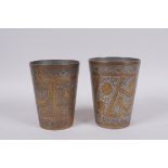 A pair of Islamic chased and gilt white metal beakers with script and floral decoration, 12cm high