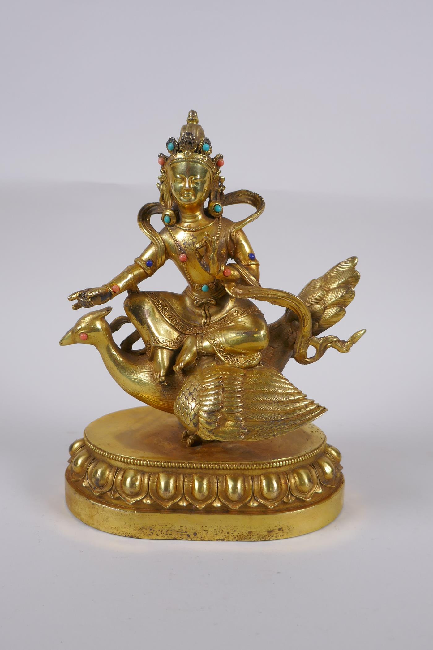 A Sino Tibetan gilt bronze figure of Buddha seated on the back of a phoenix, with inset coral,