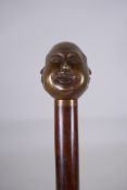 A bronze handled walking stick with a Buddha head handle, 92cm long