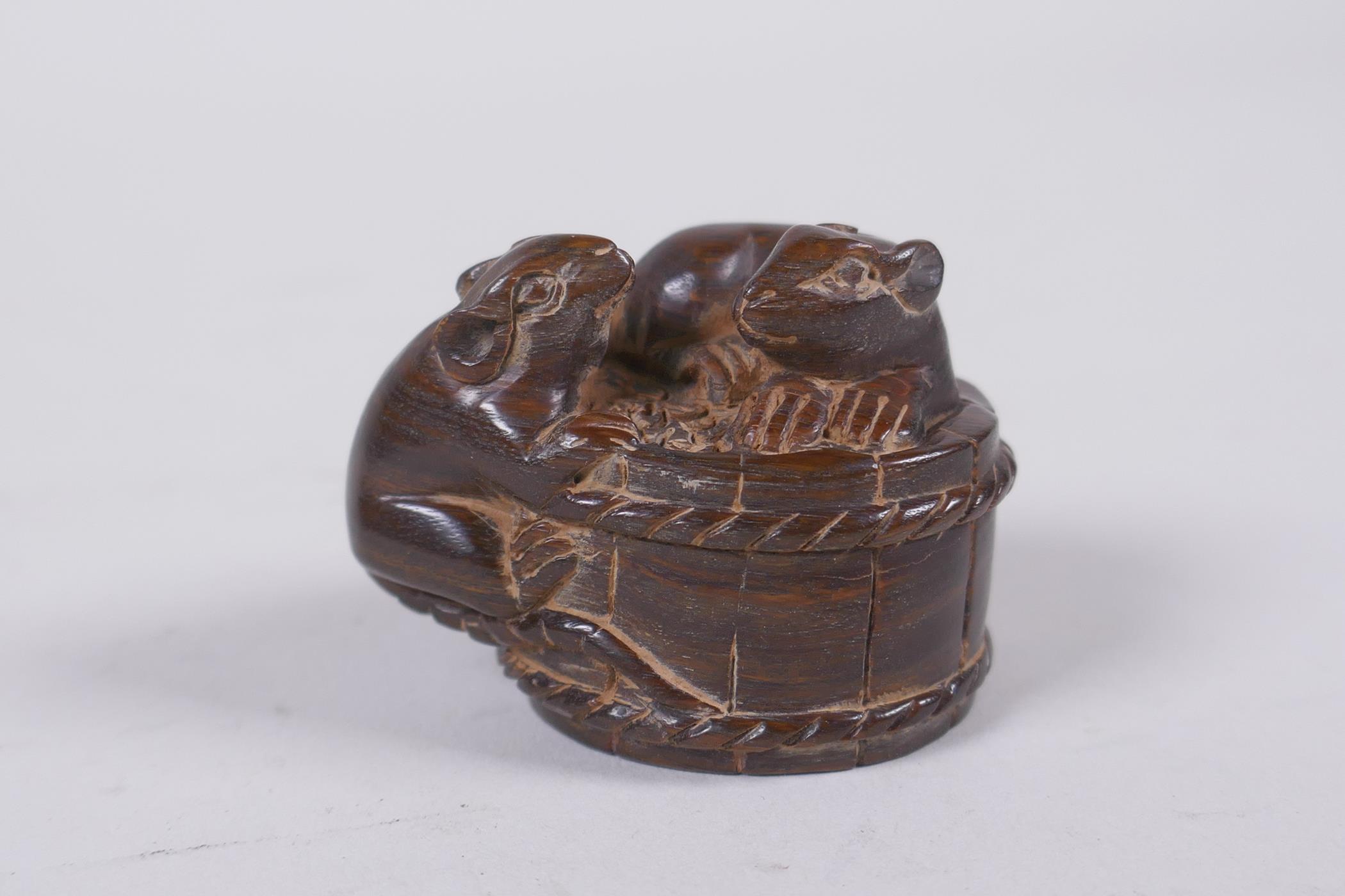 A Japanese carved hardwood okimono in the form of rats on a barrel, the base with inset signed