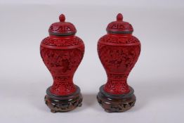A pair of Chinese cinnabar lacquer jar and covers with floral decoration, on carved hardwood