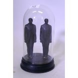 A pair of cast iron figures of standing men, mounted on a wood base and under a glass dome, 20cm