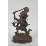 A Tibetan bronze of a sword wielding deity standing over a body, with remnants of gilt patina,