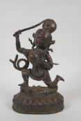 A Tibetan bronze of a sword wielding deity standing over a body, with remnants of gilt patina,