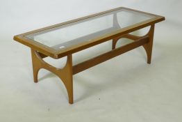 A mid century mahogany coffee table with inset glass top, raised on shaped end supports, bears label
