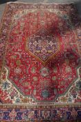 An antique Persian wool rug with medallion design on a red field with blue borders, 210 x 312cm