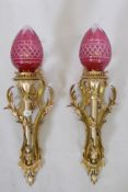 A pair of ormolu wall sconces of trumpet form with leaf swags and cranberry glass shades, 63cm high