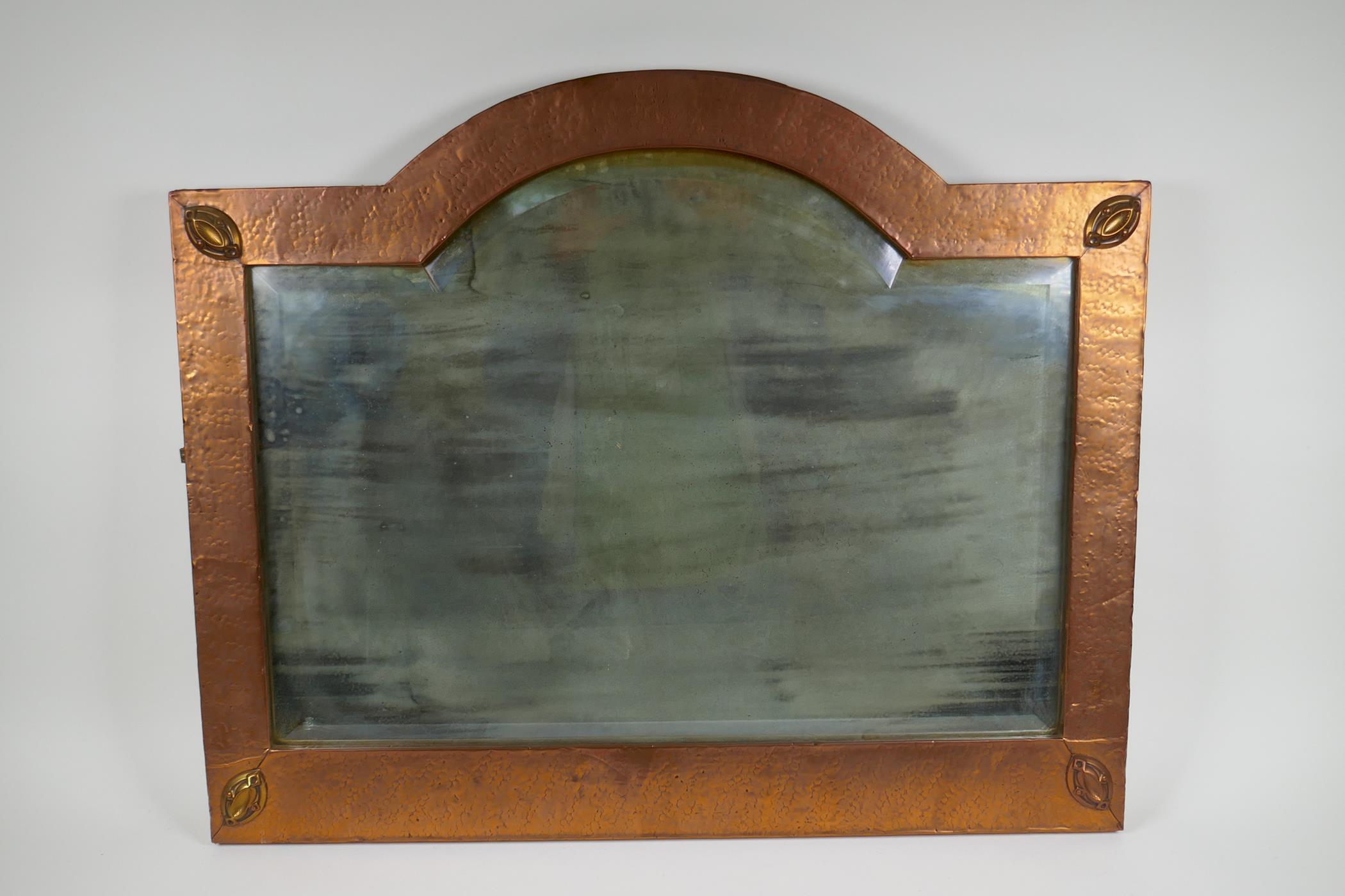 An Arts & Crafts hammered copper framed wall mirror with bevelled glass, the manner of Liberty of