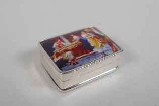 A sterling silver pill box decorated with a cold enamel plaque depicting figures in a courtyard, 3 x