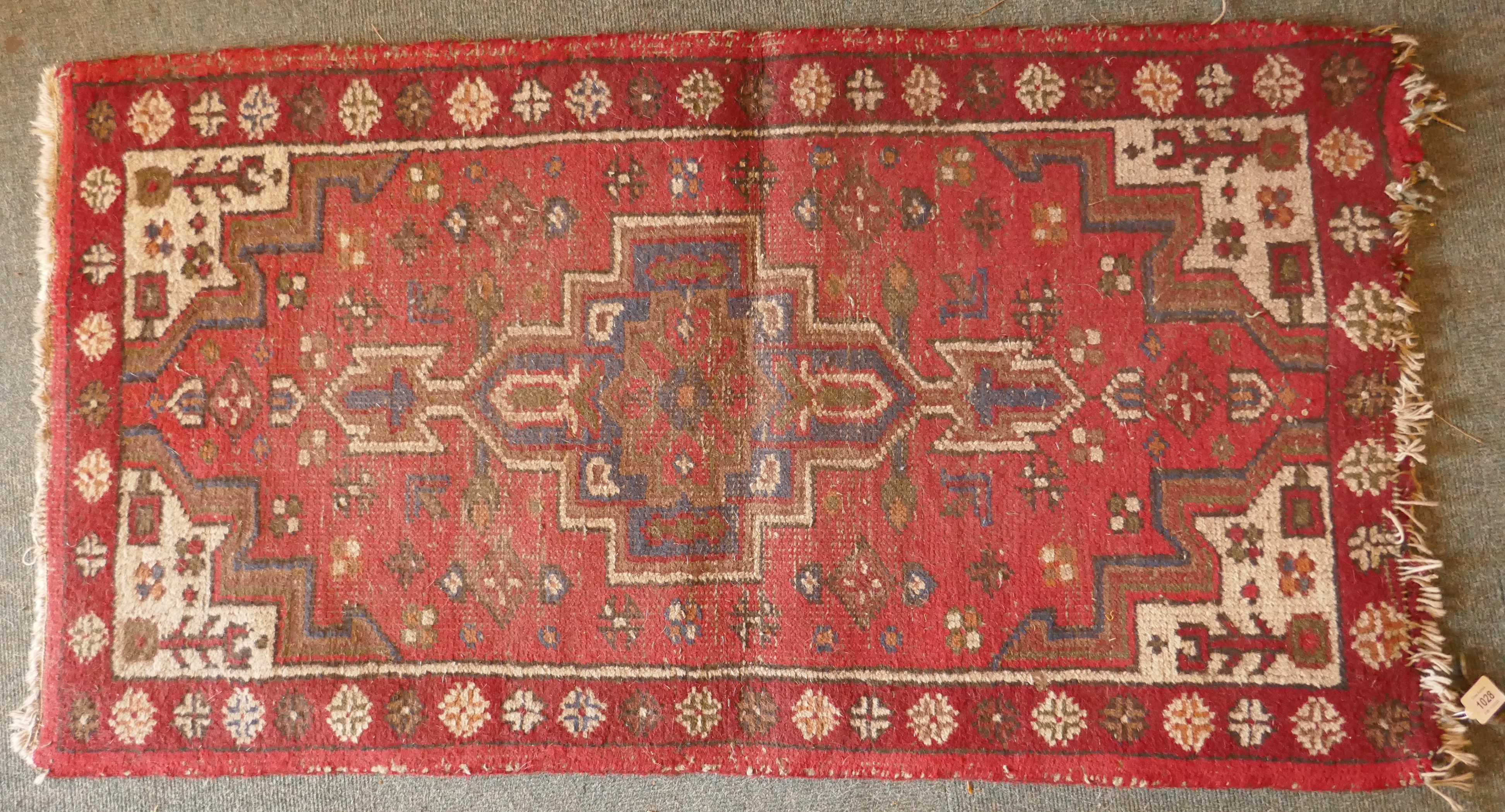 A Persian red ground wool rug with a geometric medallion design, 66 x 122cm