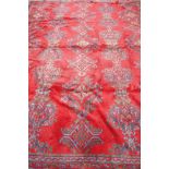 A full pile wool carpet with geometric designs on a red field, 290 x 385cm