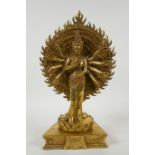 A Tibetan gilt bronze figure of a many armed deity standing on a lotus flower, 32cm high