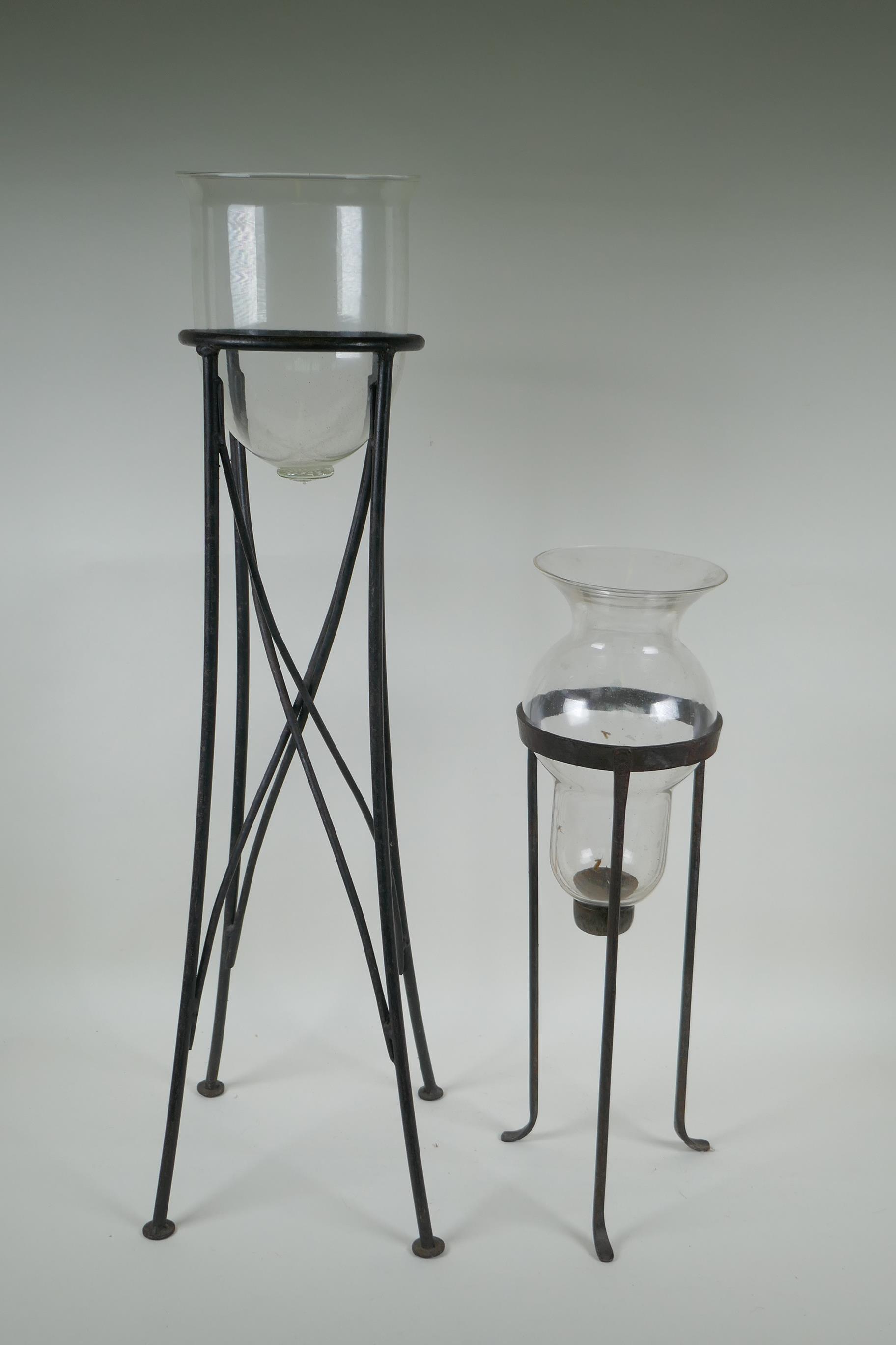 A glass hurricane vase on a wrought iron stand, and another, largest 76cm high