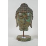 A vintage bronze Buddha's head with green patination, mounted on a stand, 27cm