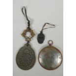 A Tibetan metal calendar, a convex mirror pendant and a cast iron skull pendant, 10cm diameter