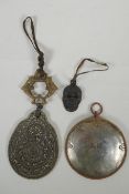 A Tibetan metal calendar, a convex mirror pendant and a cast iron skull pendant, 10cm diameter