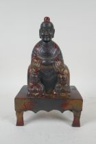 A Chinees cast metal figure of an emperor seated on a throne, with the remnants of gilt patina,