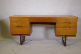 A mid century teak dressing table/side cabinet with seven drawers, raised on end supports,