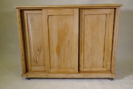A C19th pine side cabinet with three sliding doors, on a plinth base with castors, 126 x 48 x 98cm