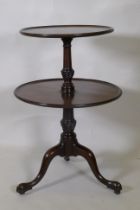 A Georgian mahogany two tier dumb waiter, raised on carved and turned column and tripod supports