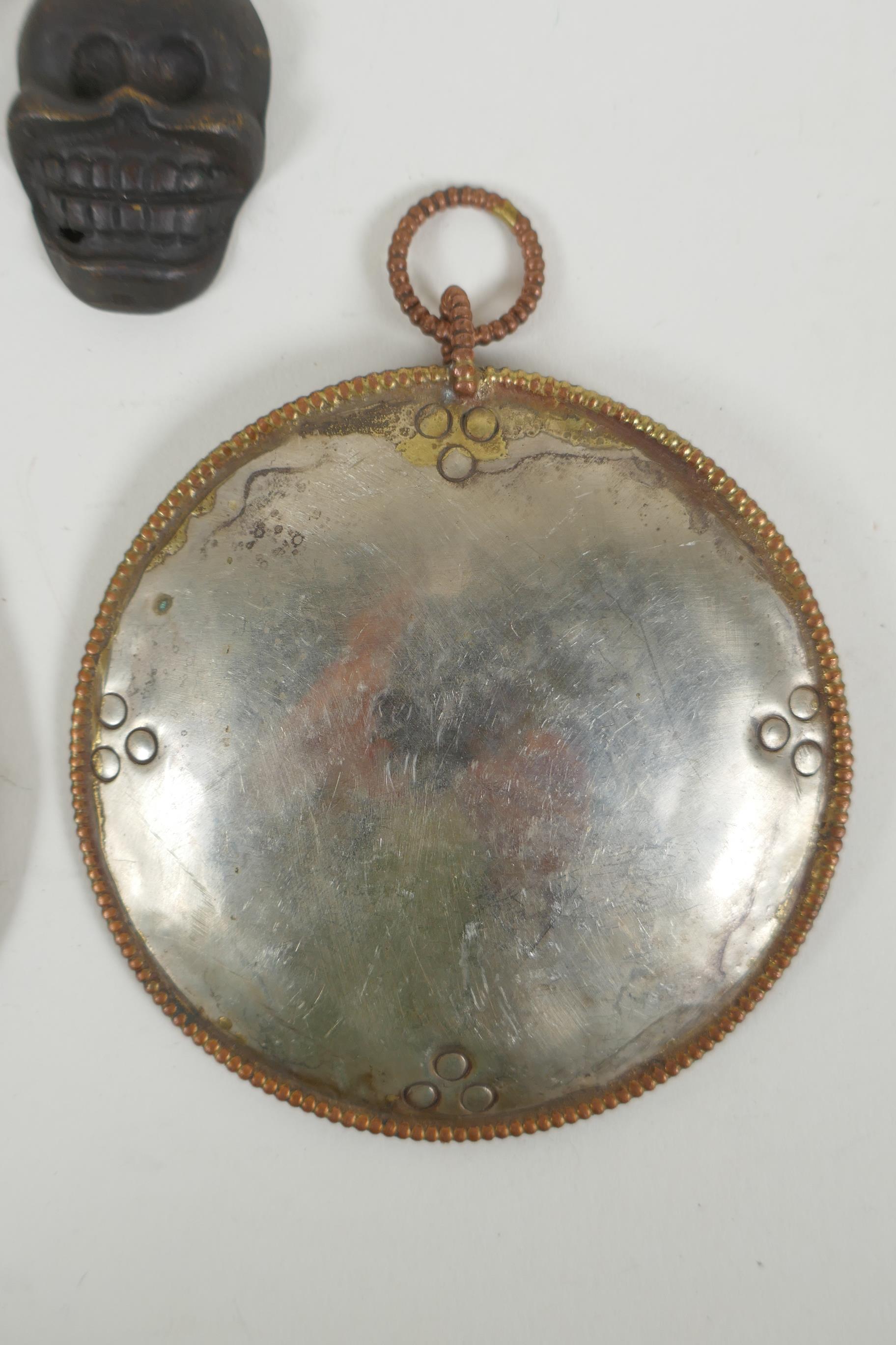 A Tibetan metal calendar, a convex mirror pendant and a cast iron skull pendant, 10cm diameter - Image 4 of 5
