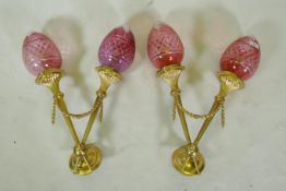 A pair of ormolu two branch wall sconces of trumpet form with cranberry glass shades, 56cm high