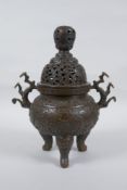 A Chinese bronze censer and cover on tripod supports, with two ruyi shaped handles and allover lotus