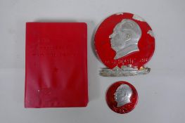 A copy of Mao's little red book, a red enamelled metal plaque depicting Mao and a similar pin, 9 x