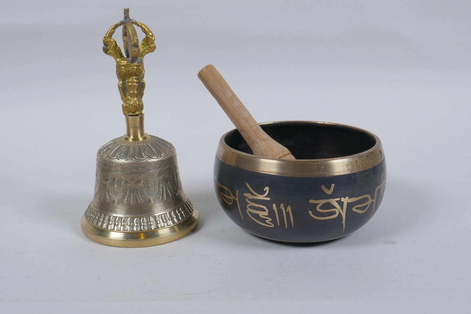 A Tibetan bronze singing bowl with script decoration and wood beater, and a brass ceremonial bell