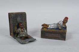 A pair of antique cold painted metal matchbox holders decorated with Arab boys on carpets, in the