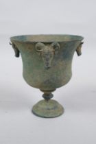 An antique metal goblet with rams head mounts, and green patina, 12cm high