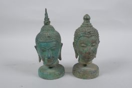A pair of bronze Buddha's heads with green patina, mounted on a metal stand, 16.5cm high