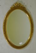 A gilt oval wall mirror with ribbon decoration and bevelled glass, 71 x 50cm