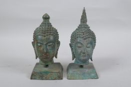 A pair of bronze Buddha's heads with green patina, mounted on a metal stand, 16cm high
