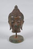 A bronze Buddha head bust on a metal base, with green patina, 25cm high