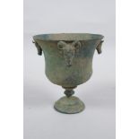 An antique metal goblet with rams head mounts, and green patina, 12cm high