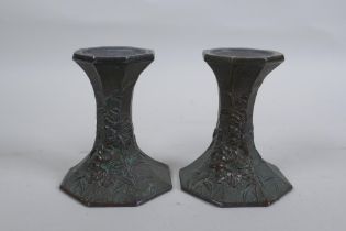 A pair of early C20th Japanese bronze candlesticks of hexagonal waisted form, with raised floral