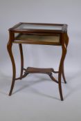 A mahogany bijouterie cabinet with shaped top, raised on splay supports united by an under tier,