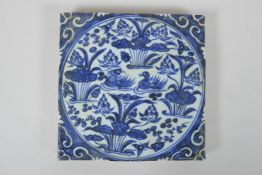 A Chinese blue and white porcelain temple tile decorated with waterfowl in a lotus pond, 20 x 20cm