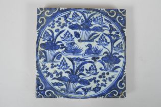 A Chinese blue and white porcelain temple tile decorated with waterfowl in a lotus pond, 20 x 20cm