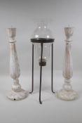 A pair of turned and distressed pricket candlesticks, and a wrought iron and glass hurricane vase,