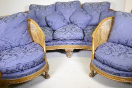 An antique walnut bergere suite comprising two chairs and settee, well upholstered, with carved
