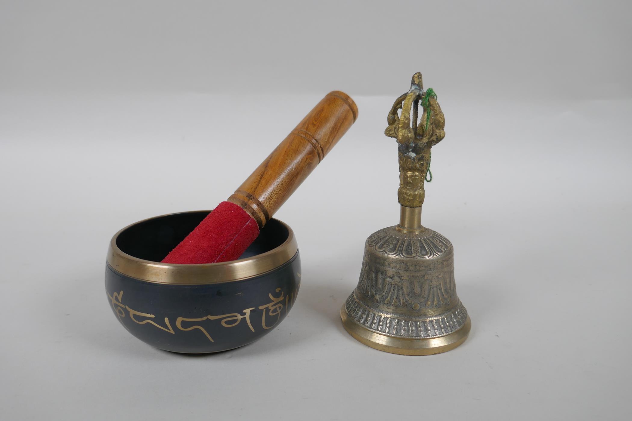 A Tibetan bronze singing bowl and beater with script decoration, a brass ceremonial bell with