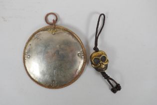 A Tibetan silvered metal mirror pendant and a bronze skull pendant, 10cm diameter