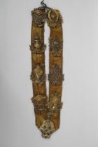 A Tibetan silk sash mounted with brass emblems depicting the Buddhist treasures, 55cm long